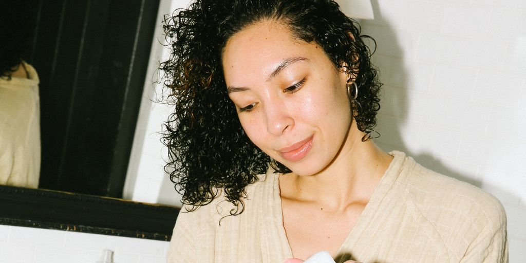 Person with skincare products near sink, smiling, casual atmosphere.