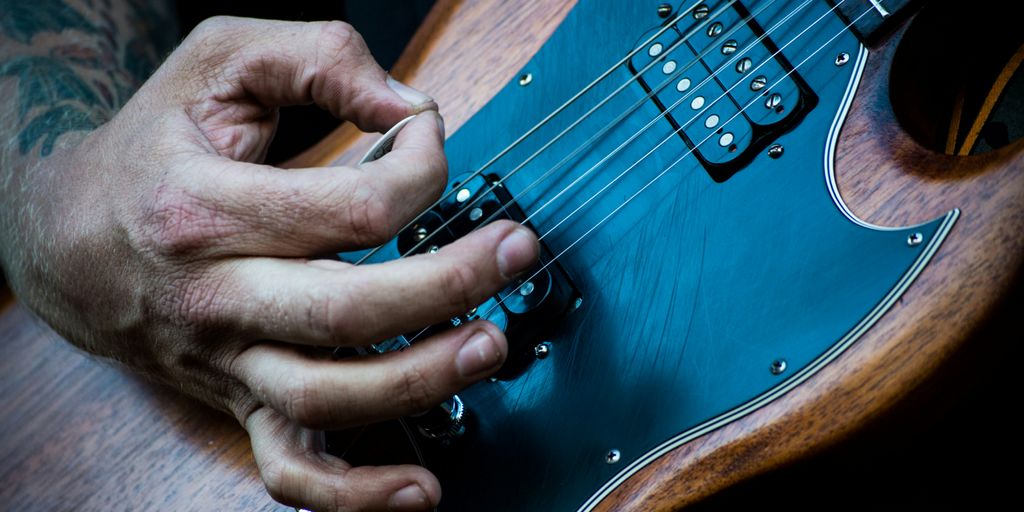 person plucking electric guitar with guitar pick