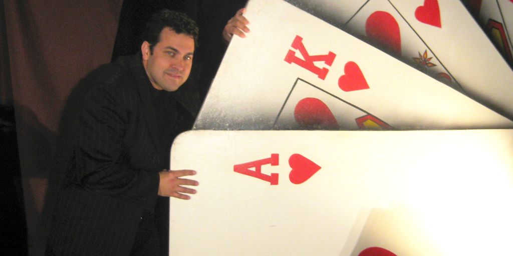 A person stands beside oversized playing cards, featuring hearts.