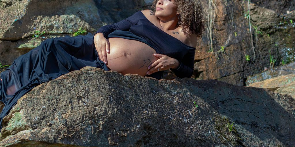 woman in black tank top and black pants sitting on rock near river during daytime