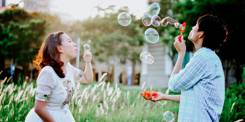 girl and man blowing bubbles near grass at daytime