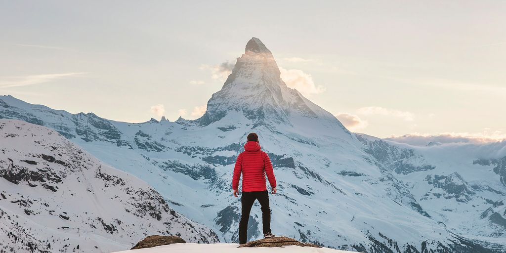 person in red hoodie standing on snowy mountain during daytime