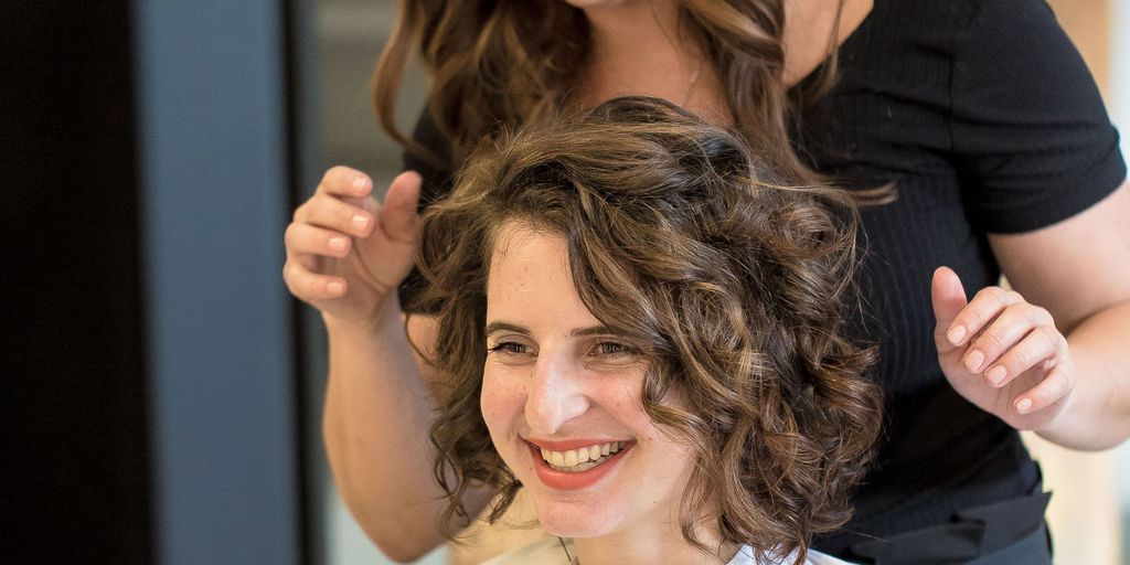 Hairstylist showcasing finished curly hairstyle on happy female client.