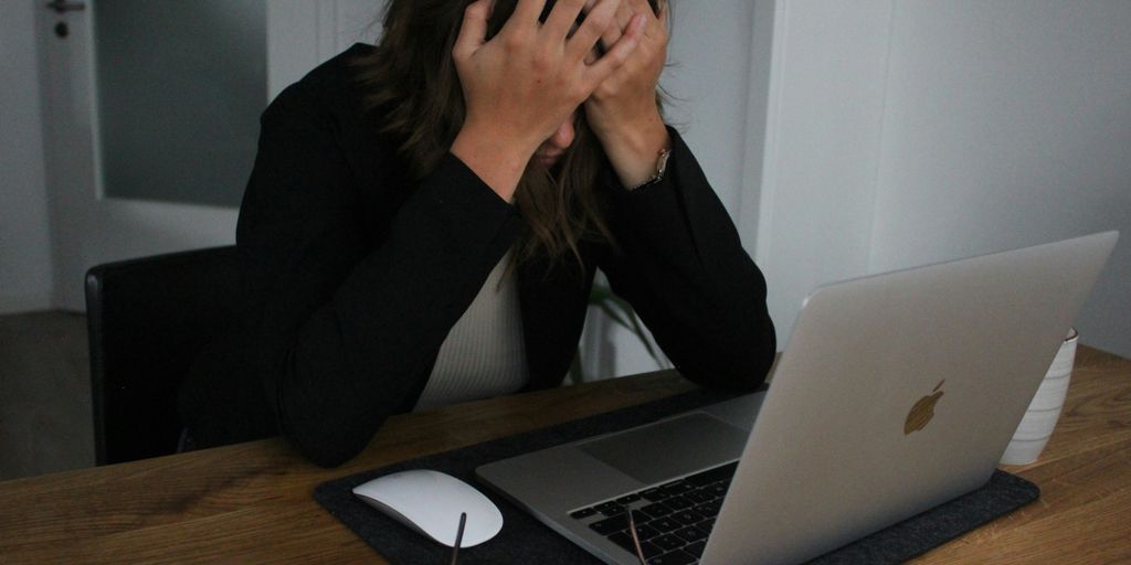 a woman covering her face while looking at a laptop