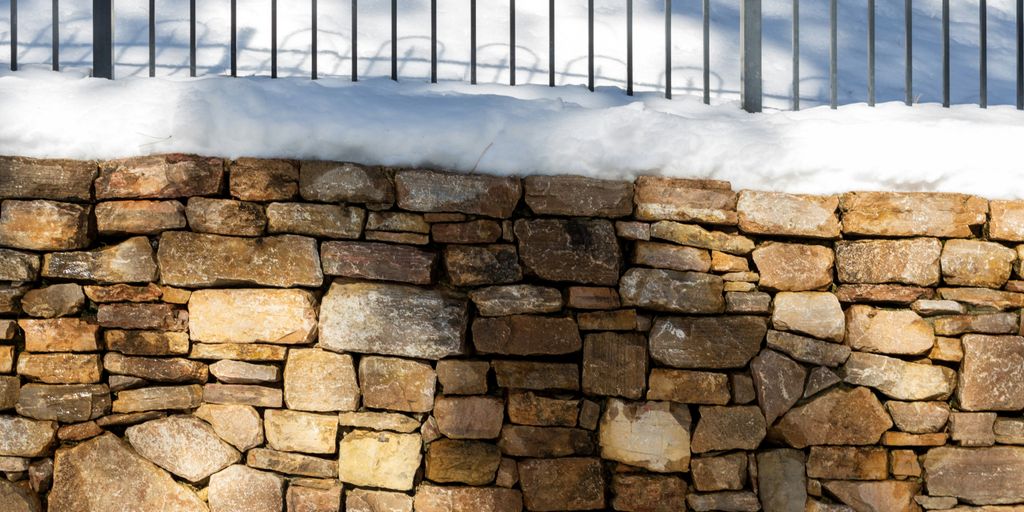 a stone wall covered in snow next to a fence