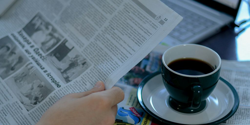 a person reading a newspaper with a cup of coffee