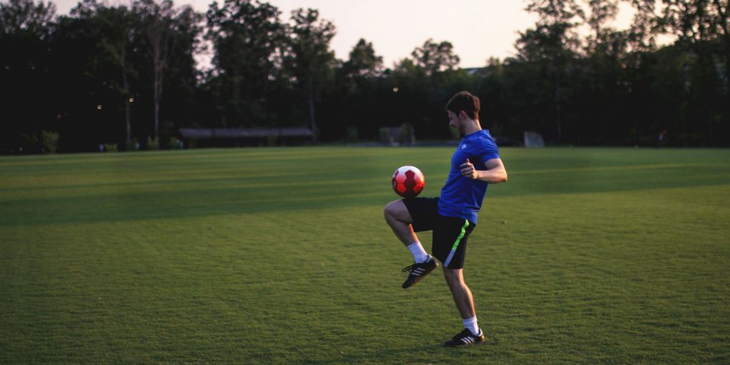 man juggling ball on grass field