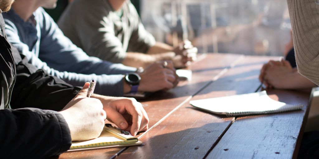 people sitting on chair in front of table while holding pens during daytime