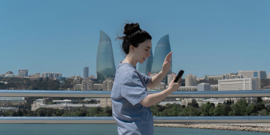 Woman waves during a video call with city skyline.