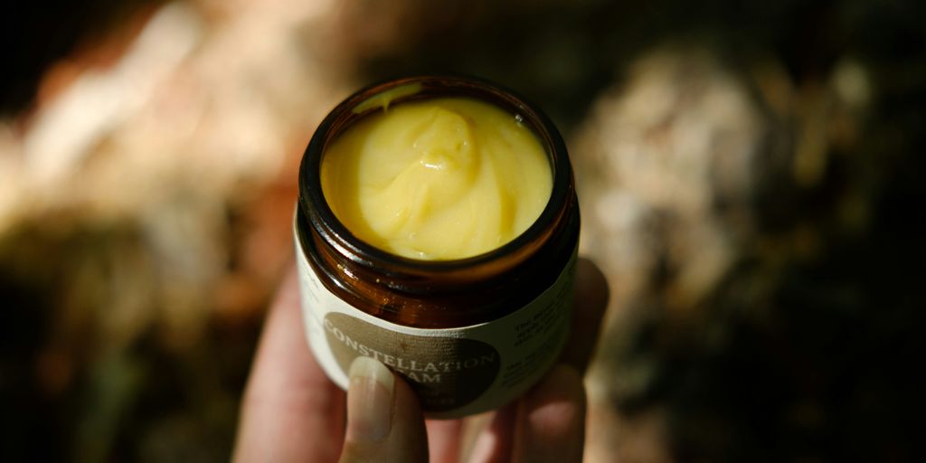 A hand holding a small jar of cream