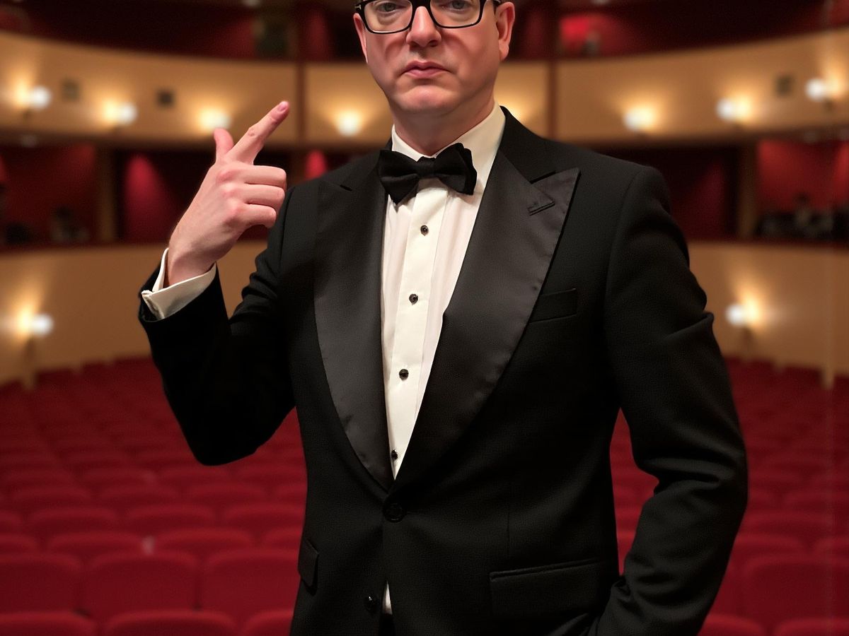 Person in tuxedo posing confidently in a theater setting.