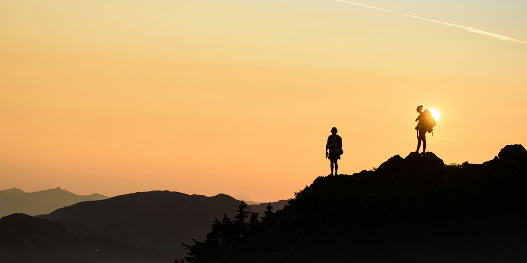 silhouette of person standing on rock formation during sunset