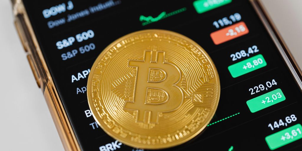 Bitcoin coin on a smartphone displaying stock market data.