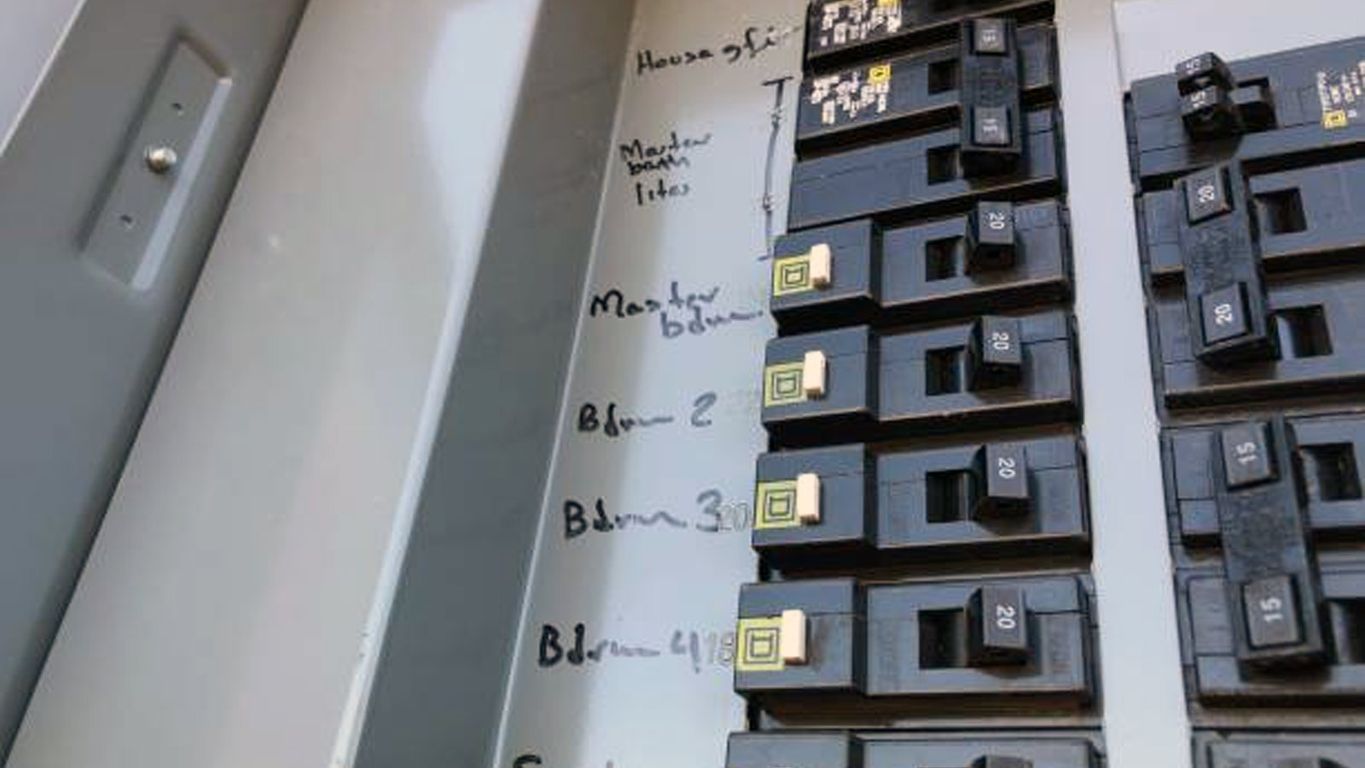 Electrical panel with labeled circuit breakers for different areas.