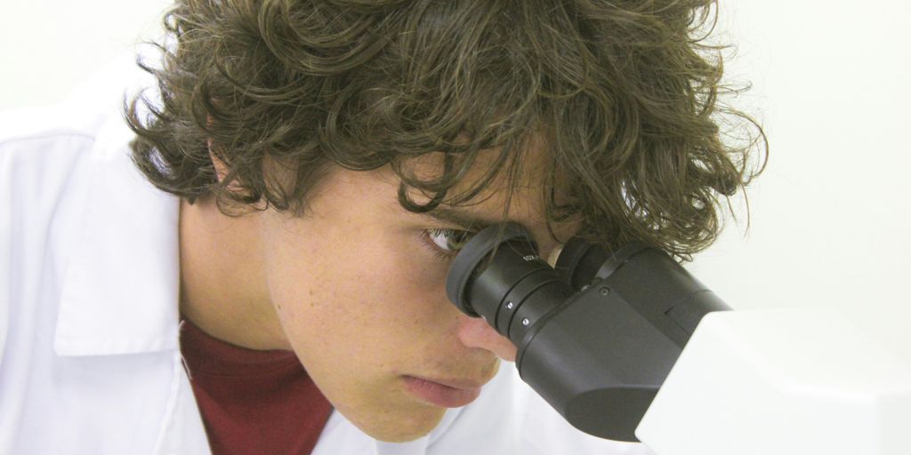 A young scientist examines through a microscope.
