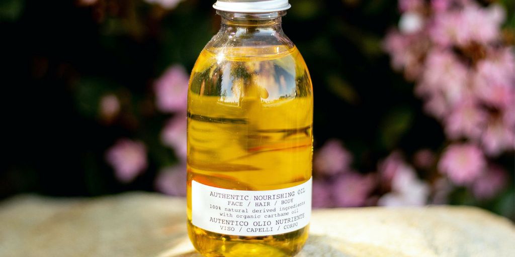 Small bottle of golden oil with flowers in the background.