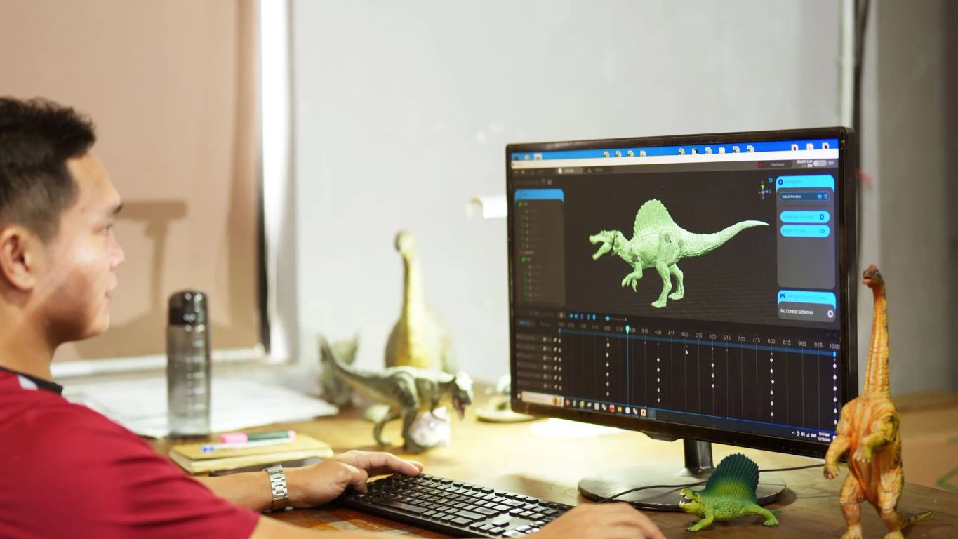 Person working on computer with dinosaur models and animation software.