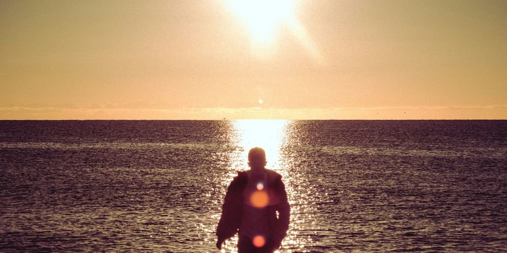 man in black wet suit standing on sea shore during sunset