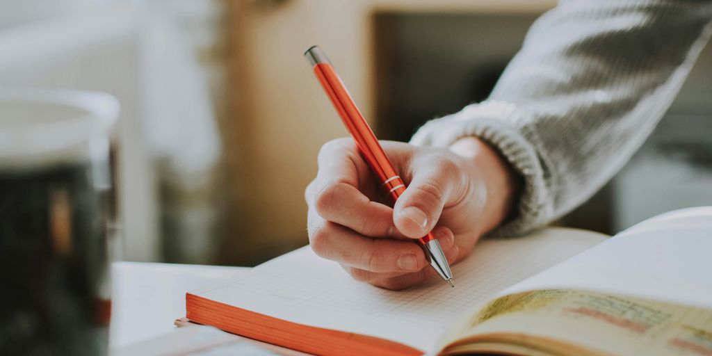 person holding on red pen while writing on book