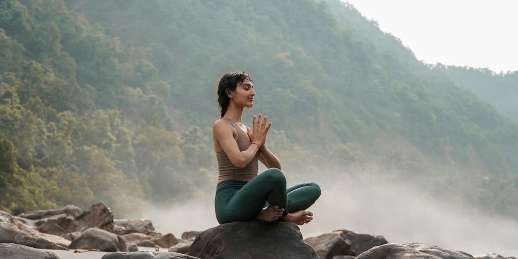a woman sitting on top of a rock next to a river