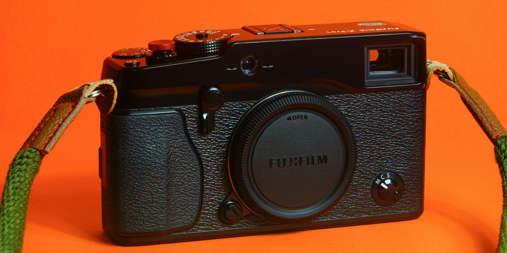 A black camera with a green strap on an orange background