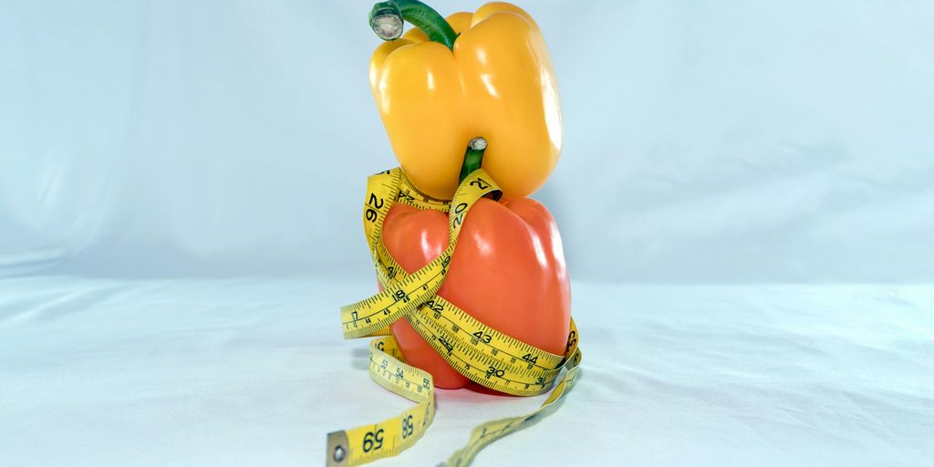 a bell pepper and a yellow bell pepper wrapped in a measuring tape