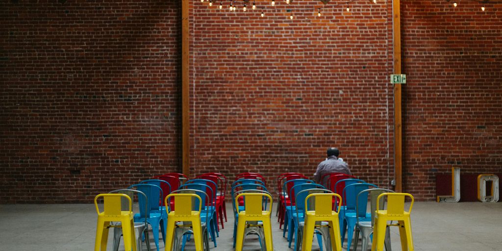 man sitting on red chair in front of brown concrete brick wall