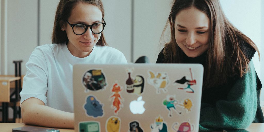 a couple of women sitting at a table with a laptop