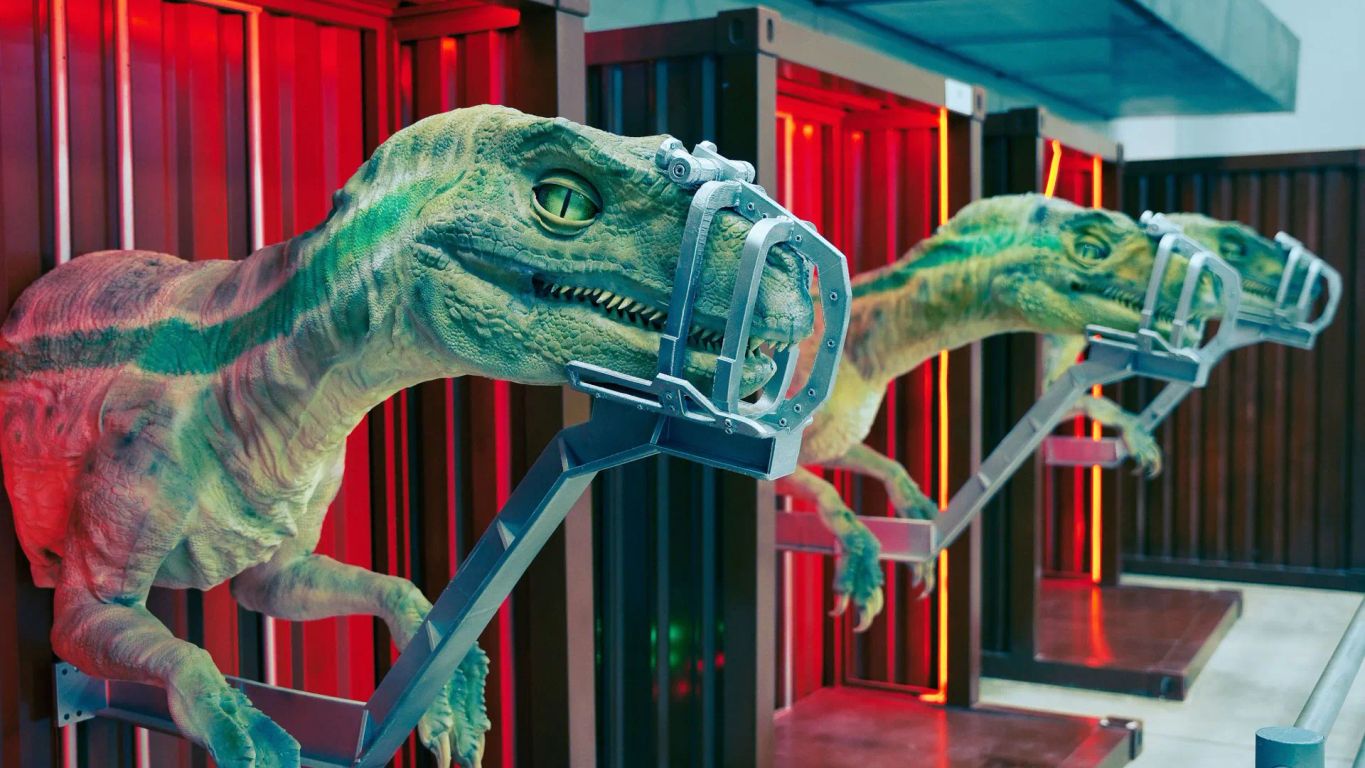 Three dinosaur-like creatures displayed in futuristic cages with red lighting.