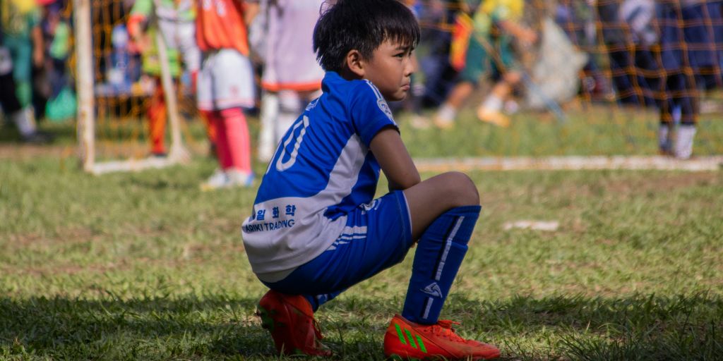 a young boy sitting on the ground during a soccer game