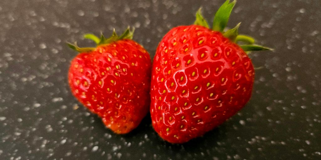 Two strawberries sitting on top of a black table