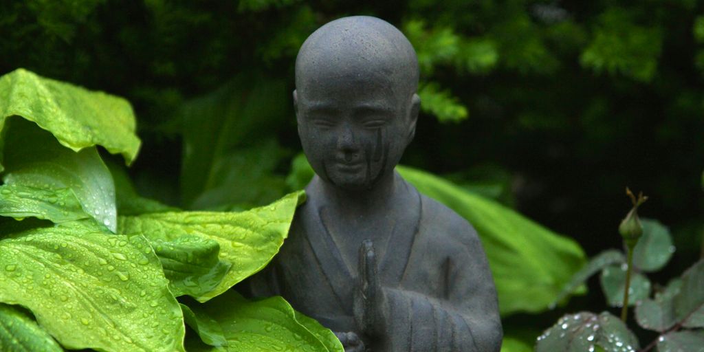 monk statue surrounded by plants outdoor during day