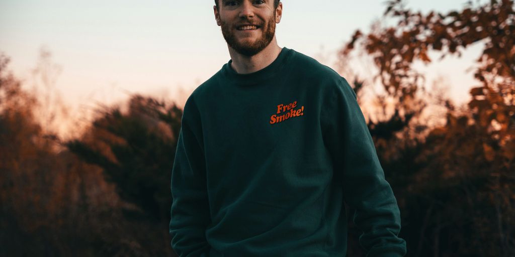 a man in a green sweatshirt standing in front of trees
