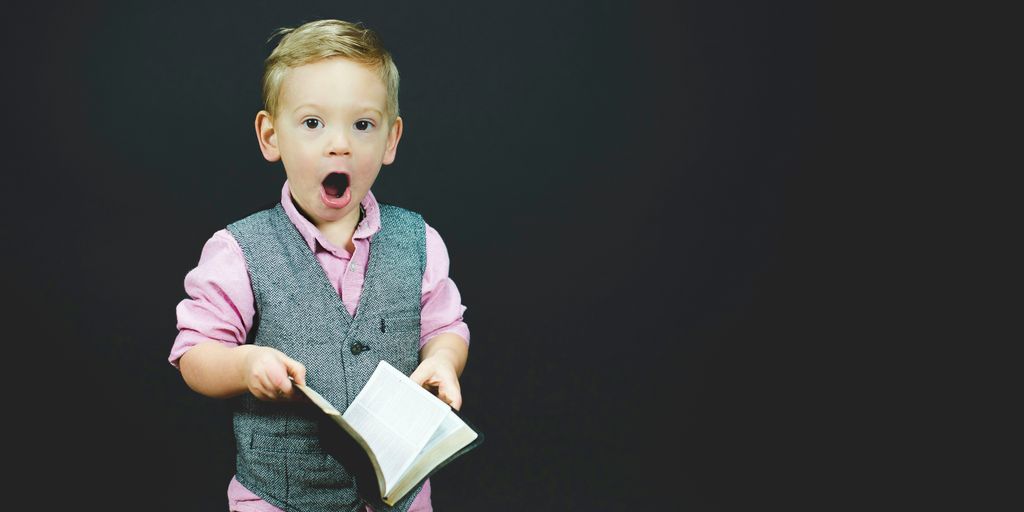 boy wearing gray vest and pink dress shirt holding book