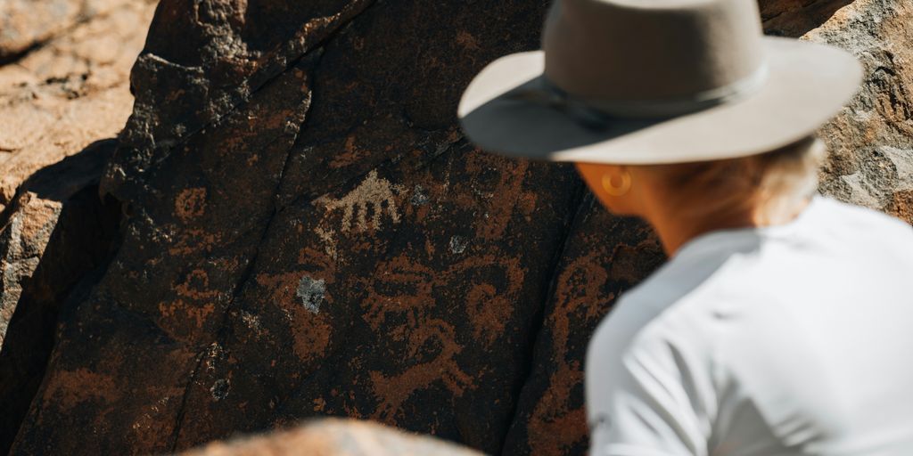 a man wearing a hat standing next to a rock