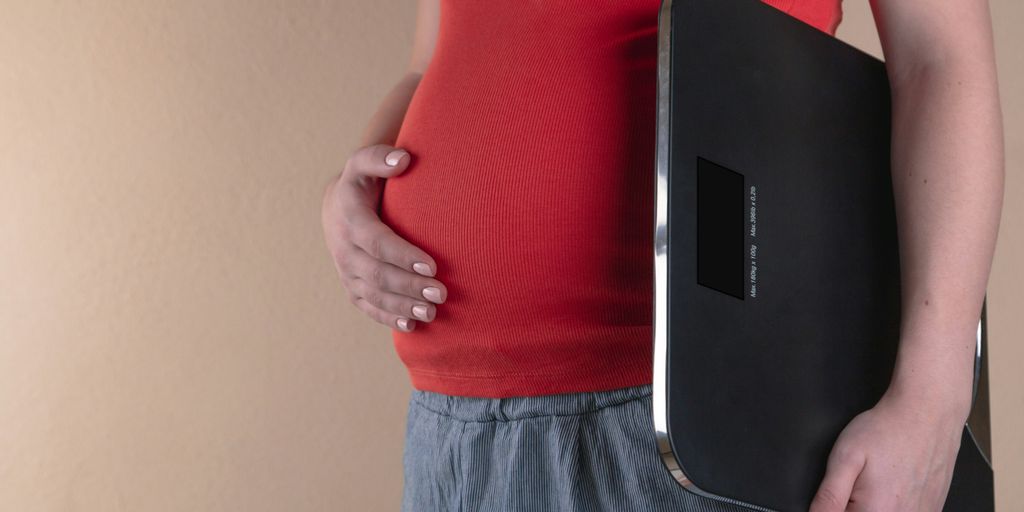 pregnant woman touching her belly and carrying a digital bathrooms cale