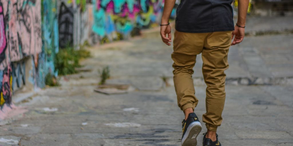 man wearing black shirt and brown pants walking beside wall with graffiti