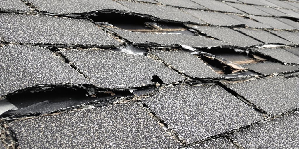 Uplifted and missing roof shingles after wind damage.