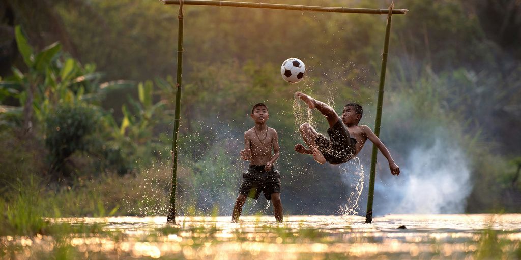 2 boys playing soccer on water during daytime