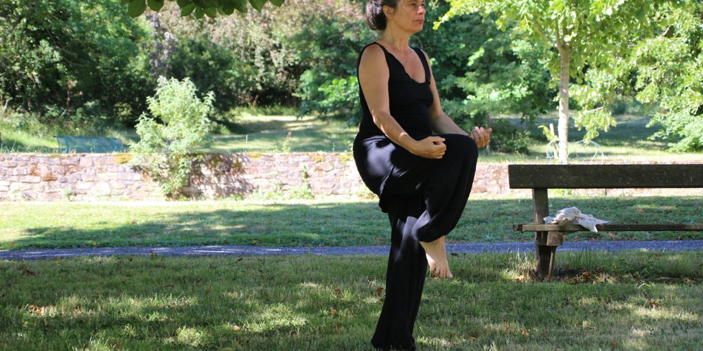 woman in black tank top and black pants sitting on brown wooden bench under green tree