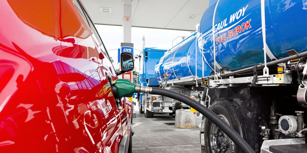 Delivery truck filling a car's gas tank.