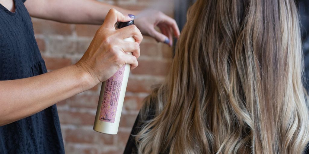 Stylist applying hair product to client's long, wavy hair.