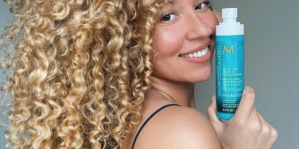 Woman showcasing a hair product with her curly hair visible.