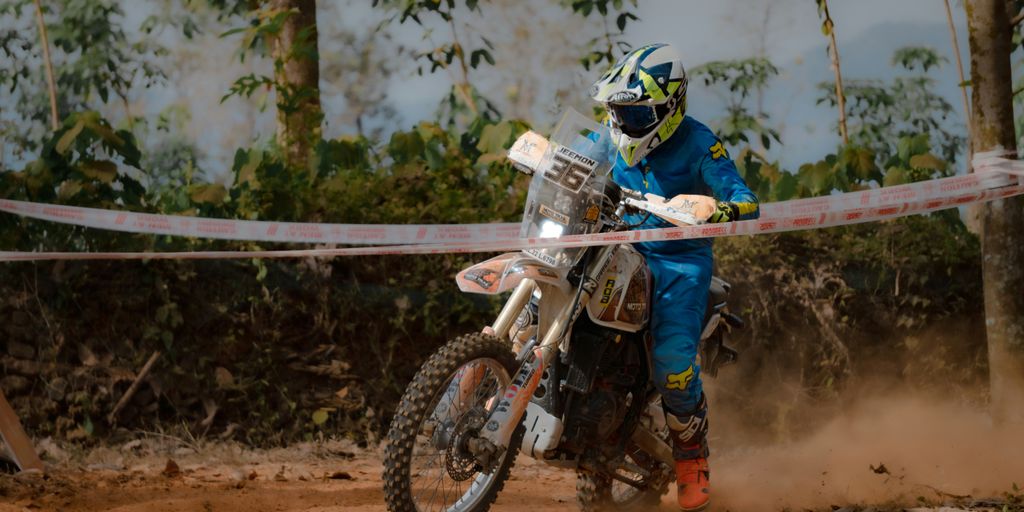 A motorcyclist races through a dusty forest trail.