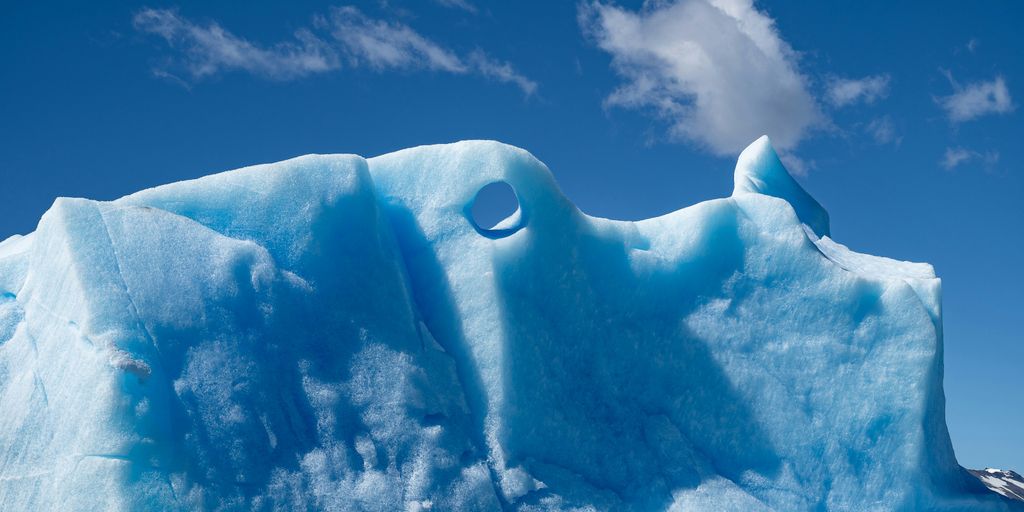 Blue iceberg floats against a blue sky.