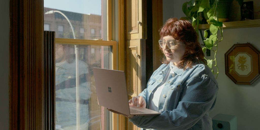 a woman standing in front of a window using a laptop computer