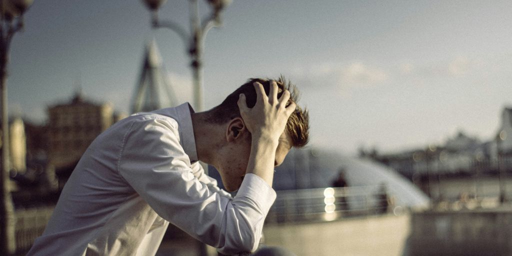 man in white dress shirt covering face with his hands