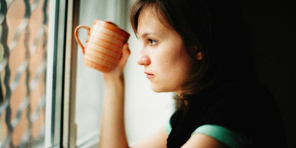 a woman holding a cup looking out a window